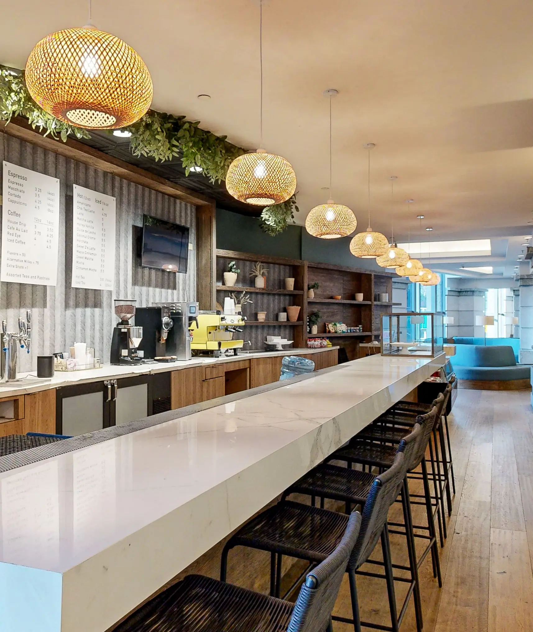 Coffee bar interior with a long white countertop bar, high stools, pendant lights, wooden shelves and espresso machines